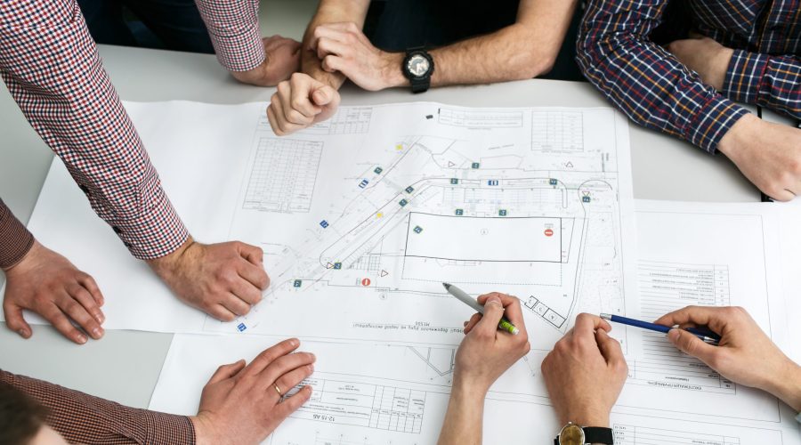 table-with-blueprints-hands-holding-pencils